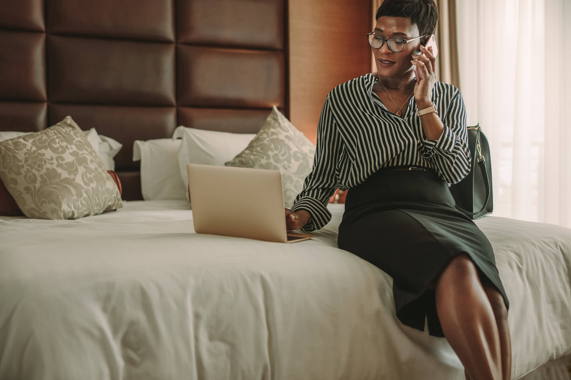 Woman in a hotel room, using the hotel's WiFi on her laptop and smartphone